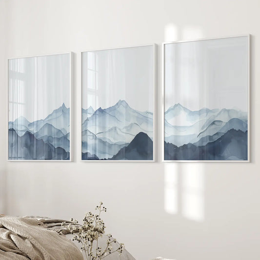 Minimalist mountain landscape triptych art, three watercolor wall prints in calming blue and gray shades. White frames over the bed.