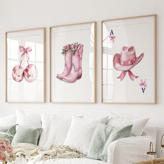 Pink Western wall art set of 3 with disco ball cherries, cowboy boots with flowers, and cowgirl hat print. Thinwood frames with mat over the couch.