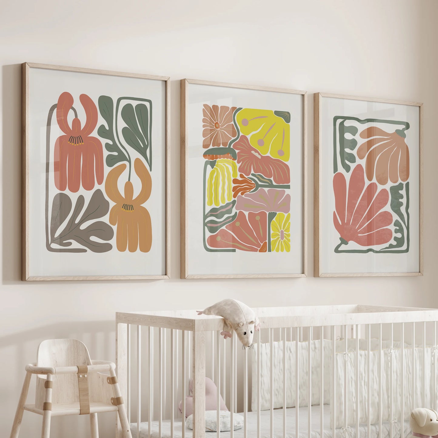 Abstract botanical florals, a print trio, float above the nursery crib in light wood frames, soft terracotta shapes creating a gentle, calming focal point.