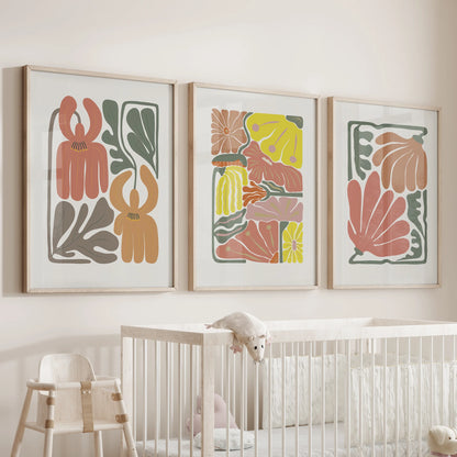 Abstract botanical florals, a print trio, float above the nursery crib in light wood frames, soft terracotta shapes creating a gentle, calming focal point.