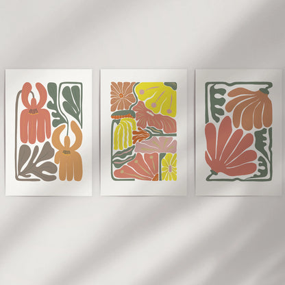 Abstract botanical florals, a set of three large loose prints, rest on a simple wall, their terracotta shapes adding warm, organic movement without frames.