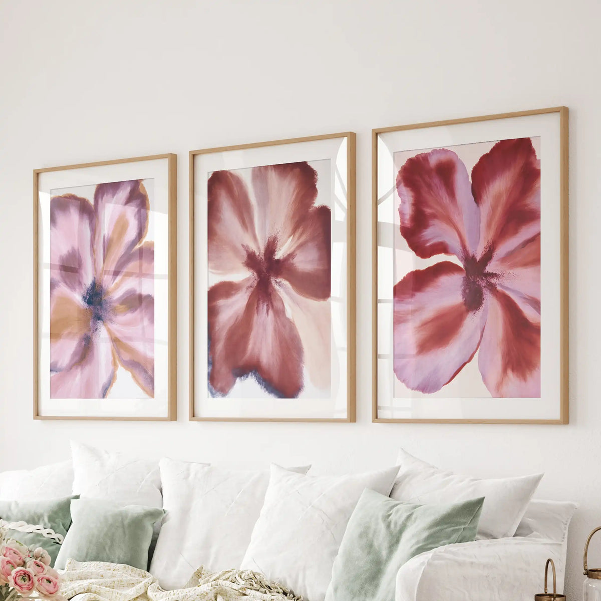 Above a sofa, matted oak frames hold three abstract burgundy flower prints.