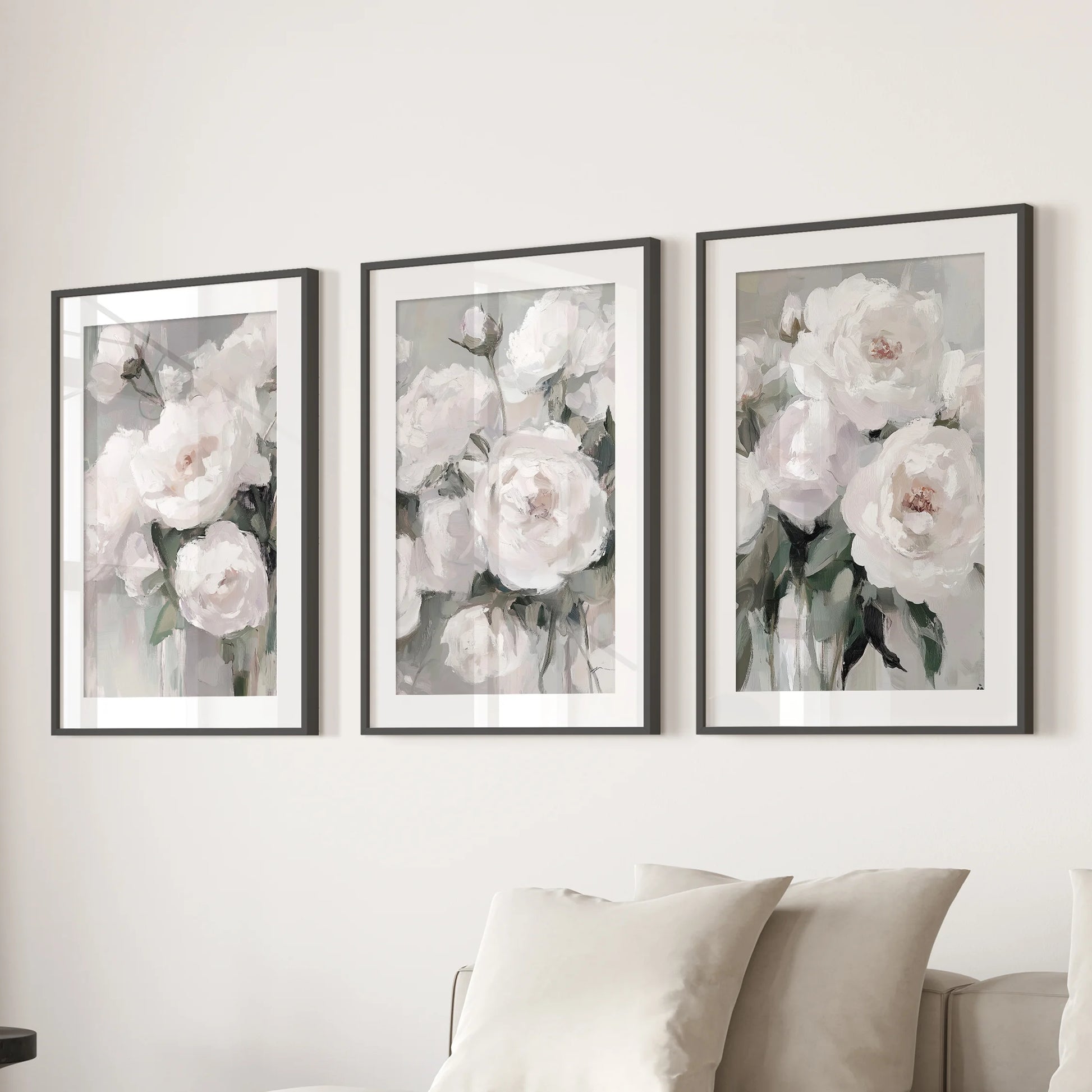 Abstract peony blossoms, a set of three wall prints in black matted frames, float over the living room sofa with soft, painterly petals and airy white space.