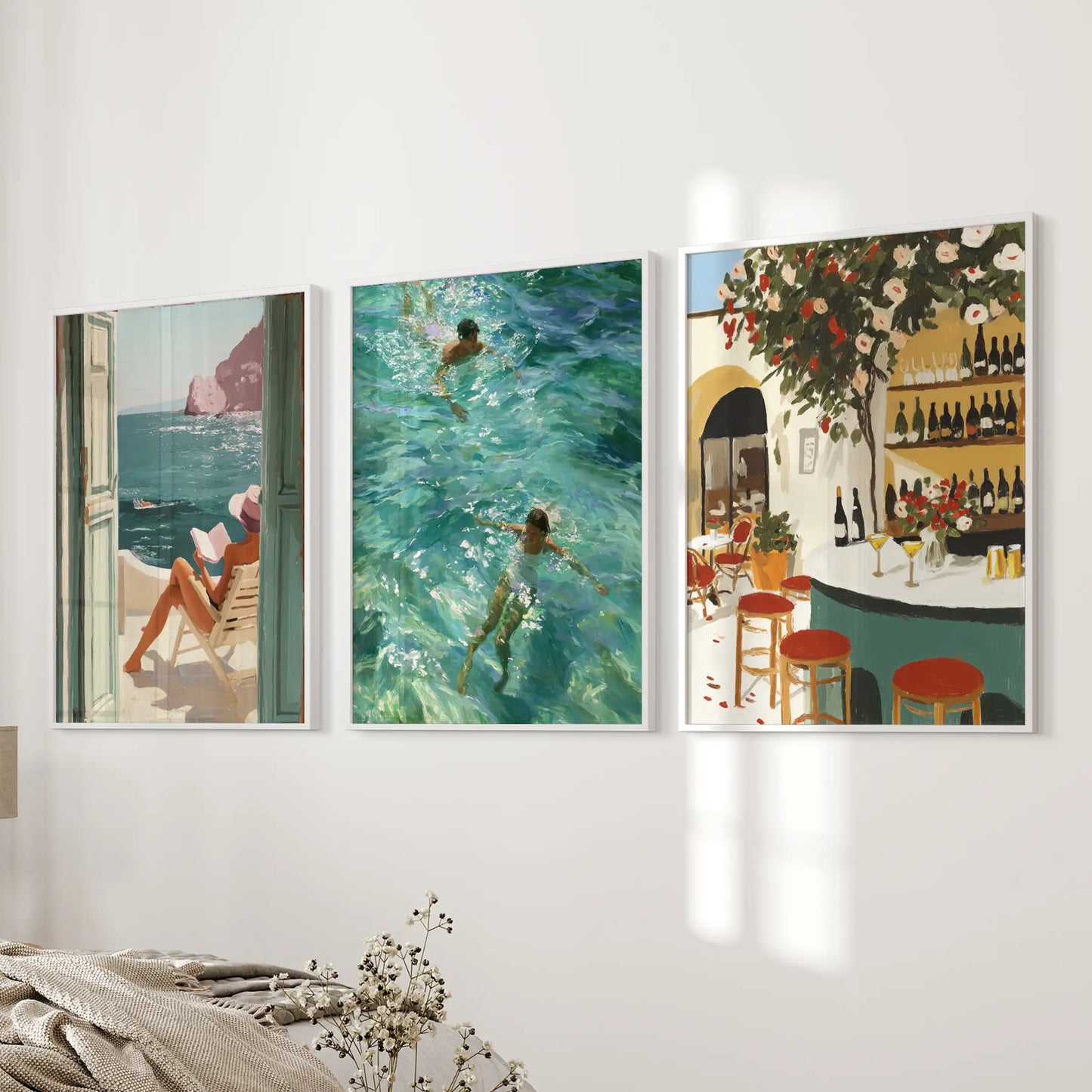 Set of three white-framed wall prints of seaside cafés spreads across the bedroom wall, lending an easy Mediterranean vibe.