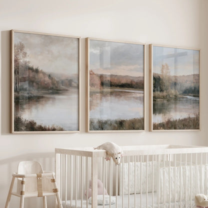 A trio of art prints with soft impressionist fall vistas rests in thin wood frames over the nursery cot, with hushed neutrals and gentle lake light.