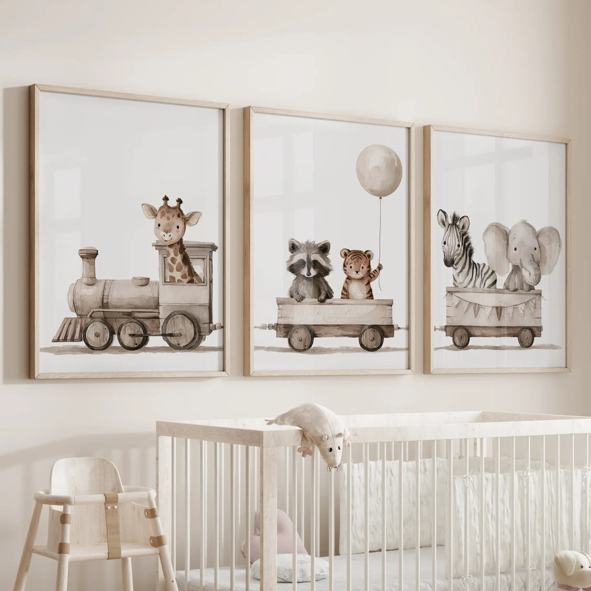 The middle of three oak-framed prints above a crib shows a raccoon and tiger beneath a balloon; a giraffe leads the train at left.