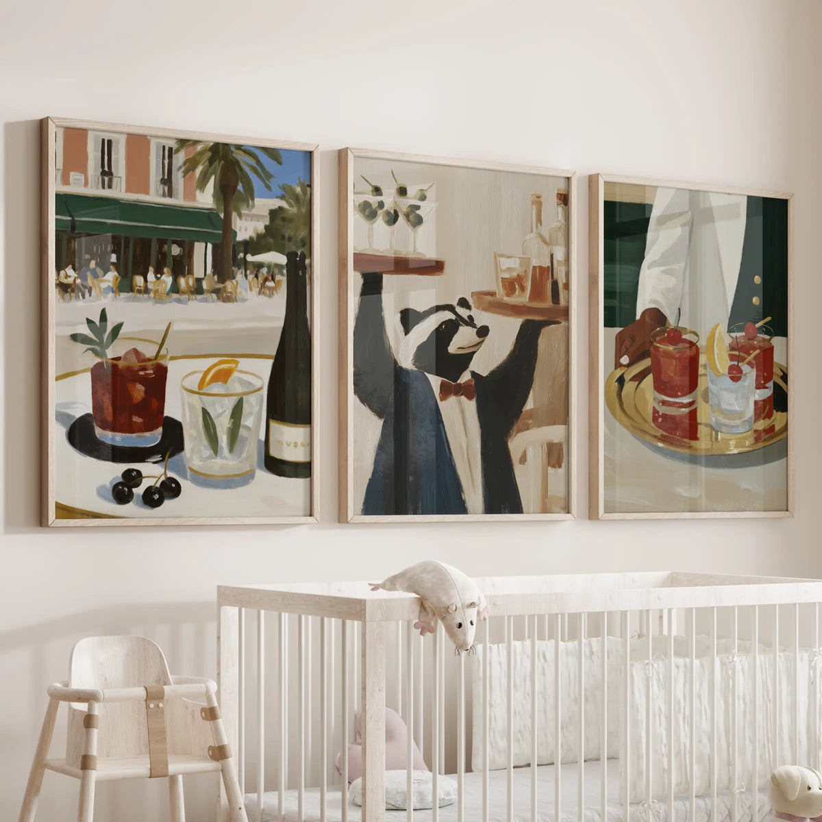 Bar cart artwork in a set of three large wall prints, shown in natural oak frames over a bassinet in a baby room.