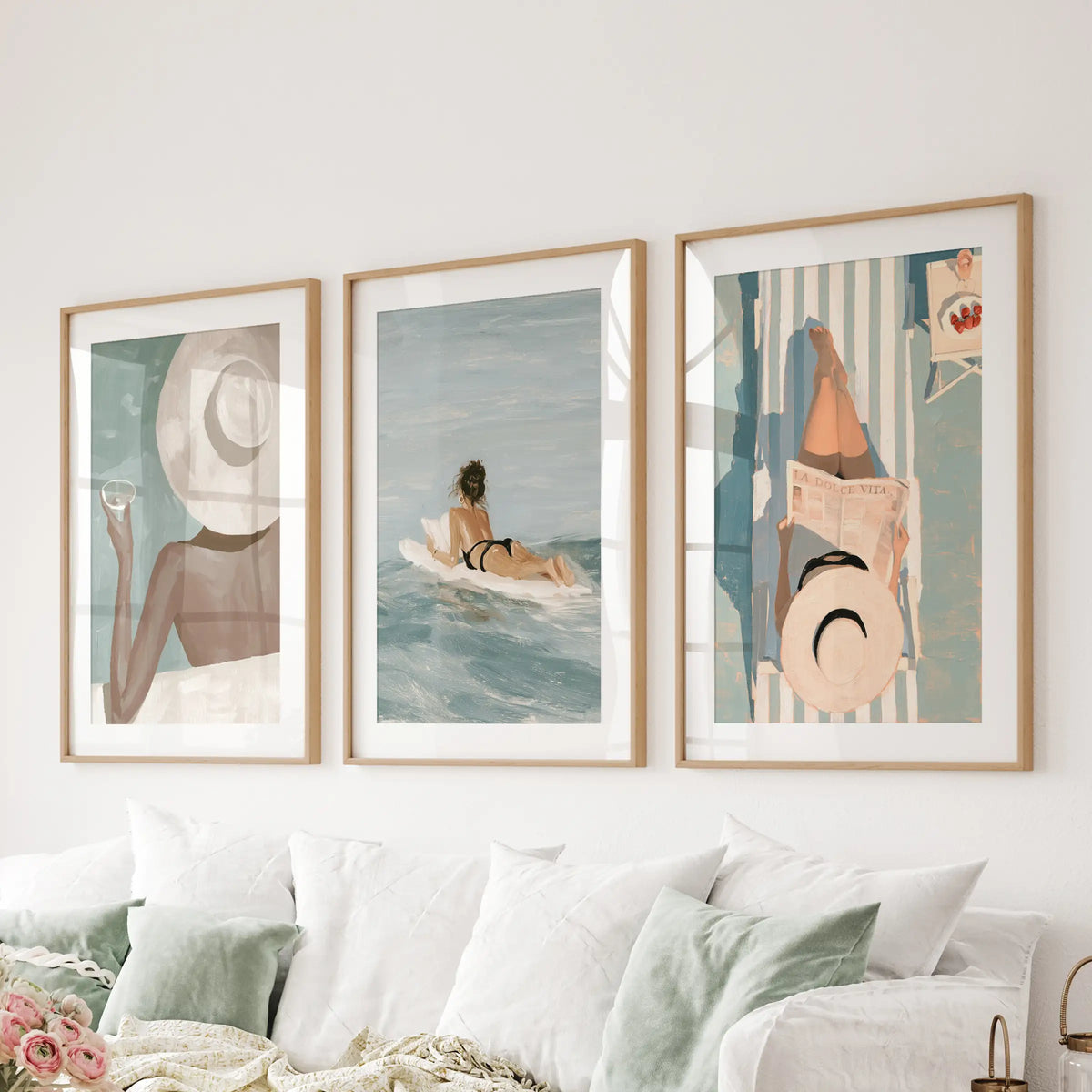 Beach girl set of three wall prints in thin wood frames with mats, hanging over a sectional in a family room.