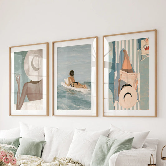 Beach girl set of three wall prints in thin wood frames with mats, hanging over a sectional in a family room.