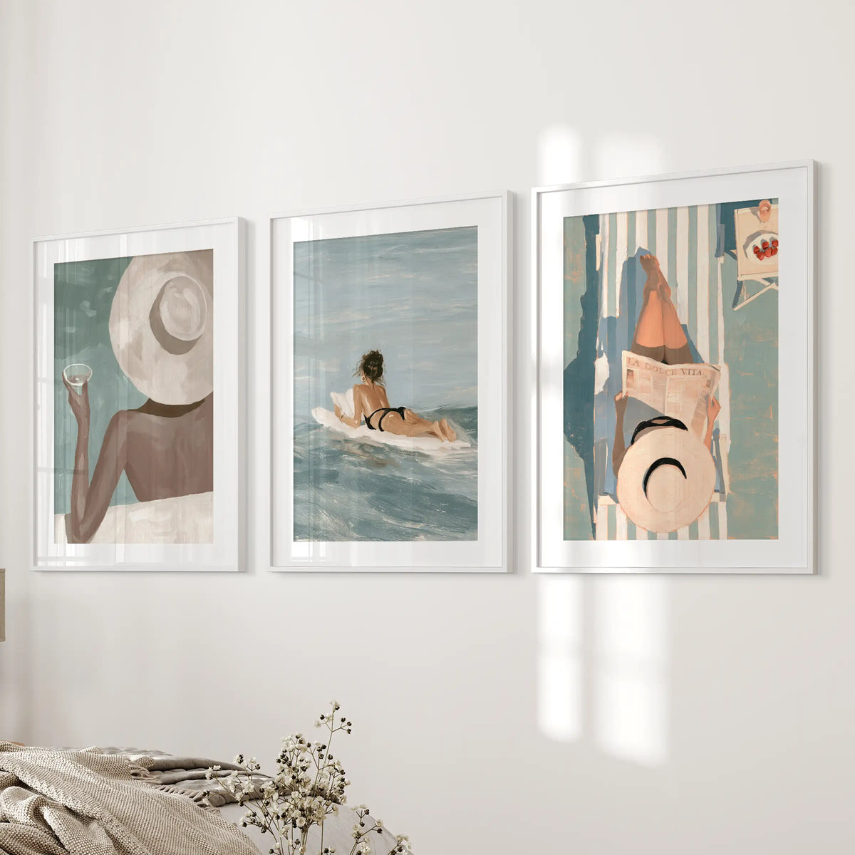 Beach girl wall art trio in white frames with mats, displayed on a bedroom wall beside the bed.