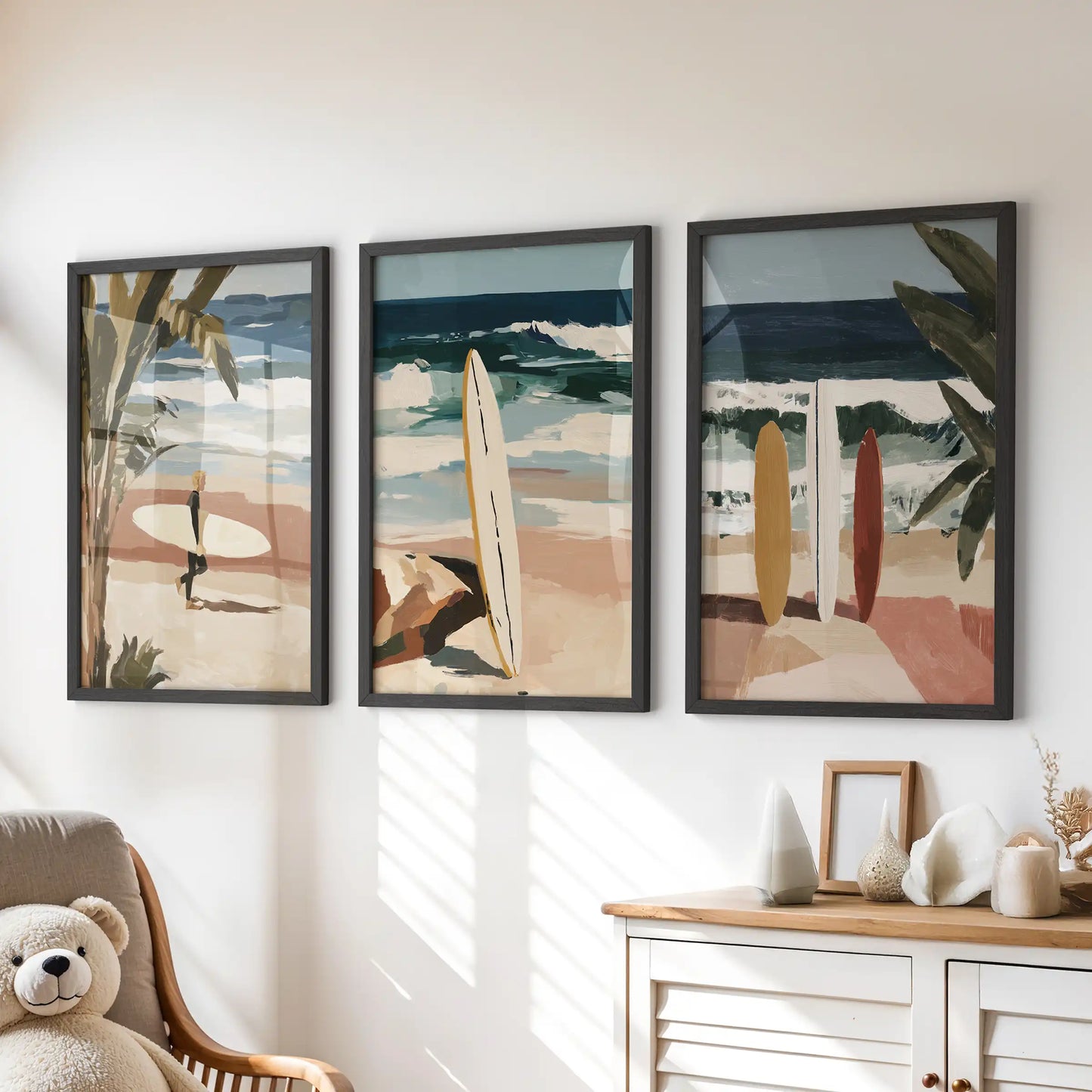 Three framed coastal beach artworks in black sit over the playroom dresser, adding sky blues and sandy neutrals to the space.