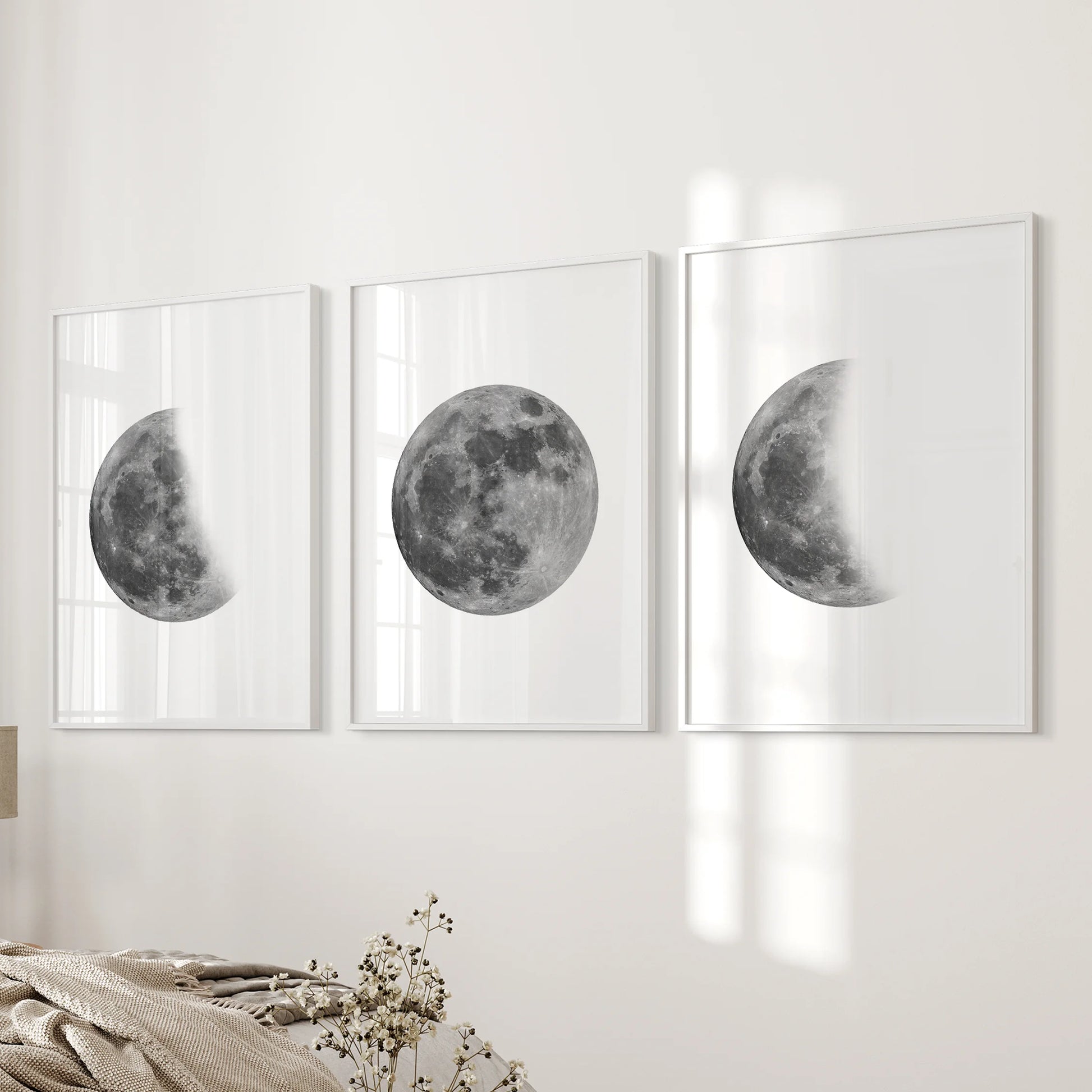 Moon phases sequence set of three prints in white frames hangs on the bedside wall, adding soft monochrome lunar art to the bedroom.