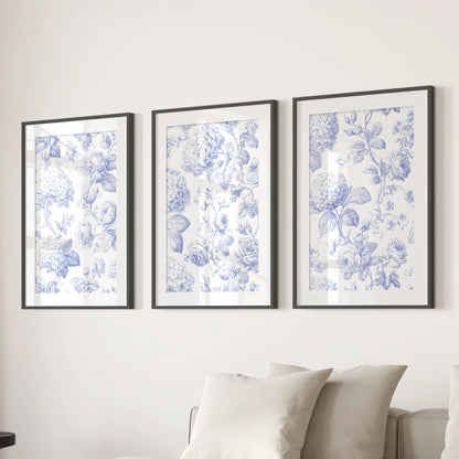 The three matted black frames above a sofa hold blue floral prints, with curling stems and leaves on warm cream backgrounds.