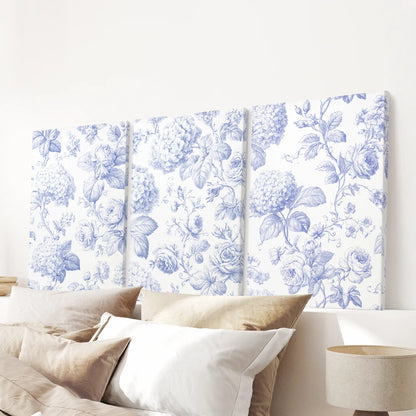 Blue roses, hydrangea heads and curling leaves fill three separate canvases above the bed pillows, against warm cream backgrounds.