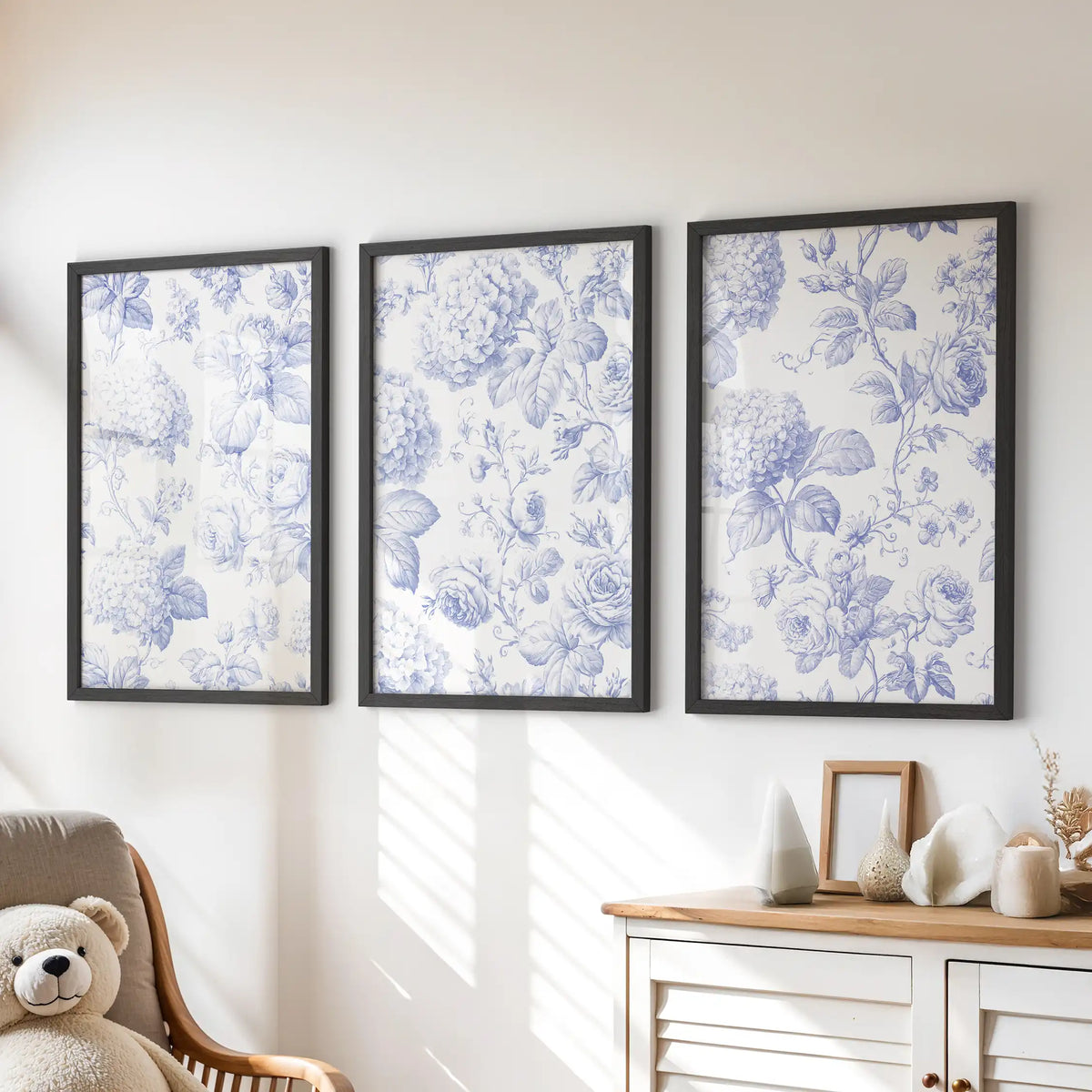Fine blue roses and hydrangea clusters fill three black-framed prints above a dresser, beside a chair with a teddy bear.