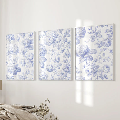 A blue floral pattern of roses, rounded flower clusters and fine leaves spans three white-framed prints beside a bed.