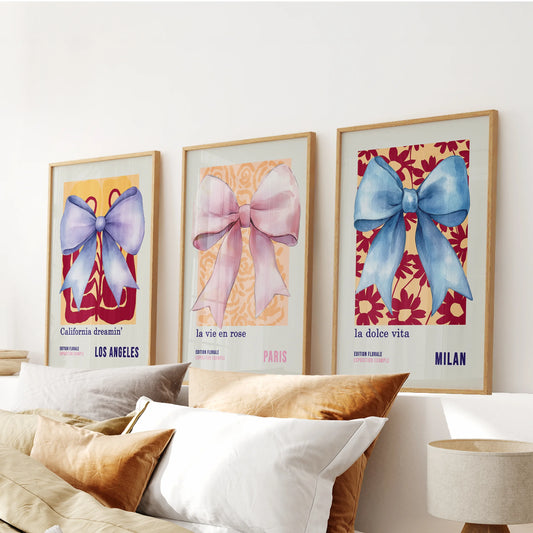 Three thin wood-framed art prints of 70s-style bows stretch above the bed, softly uniting blue and pink hues across the bedroom.