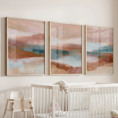 Three-piece wall artwork in oak wood frames features blush pink, terracotta and blue color fields, creating a soothing accent above the nursery cot.