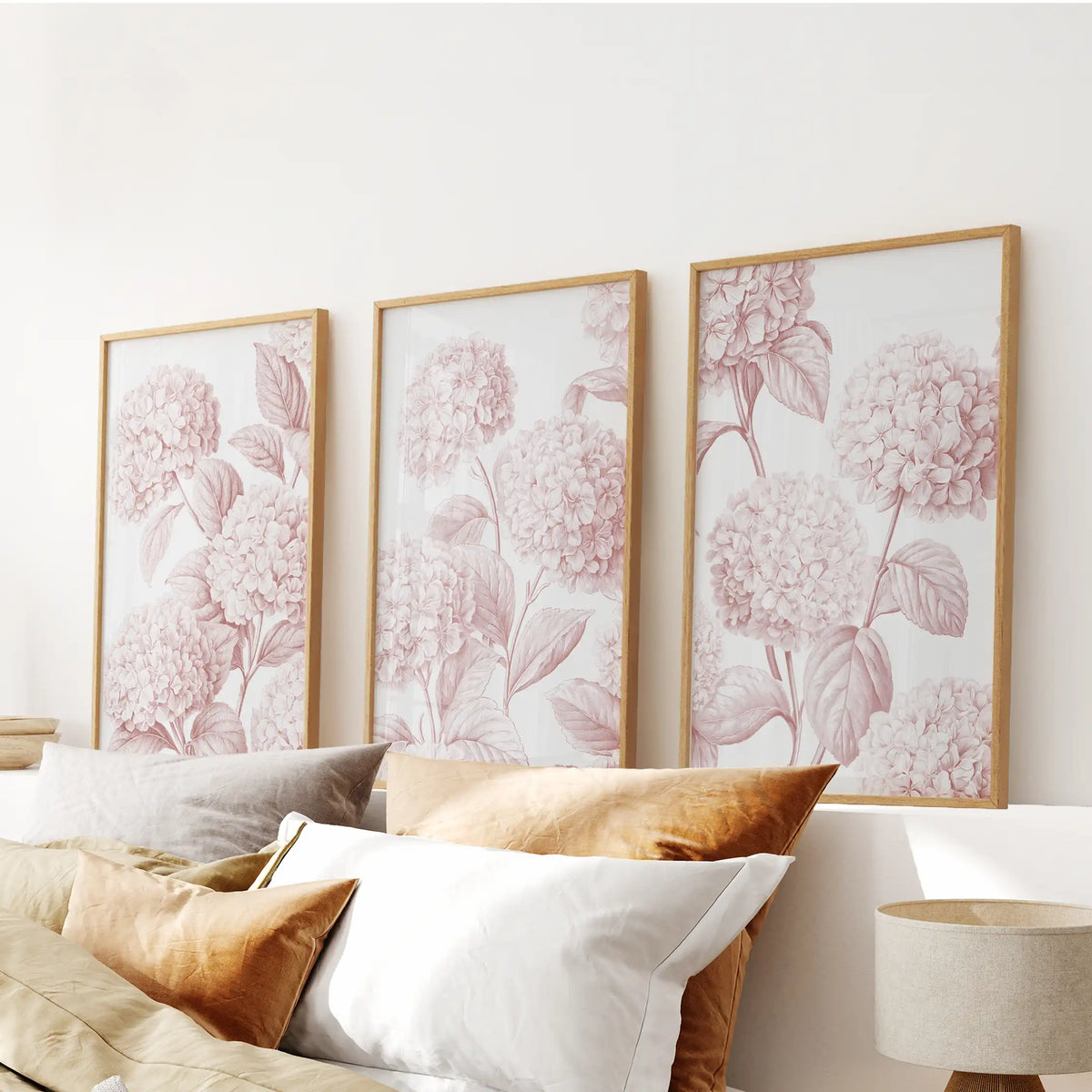 Pink hydrangea prints hang in three oak frames above a bed.