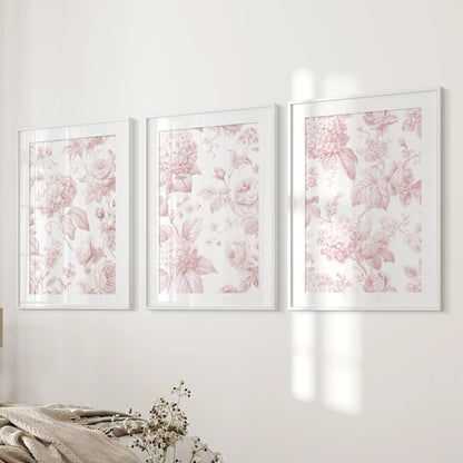White mats and frames surround three prints beside a bed, each filled with pale pink roses, hydrangea clusters and leafy stems.