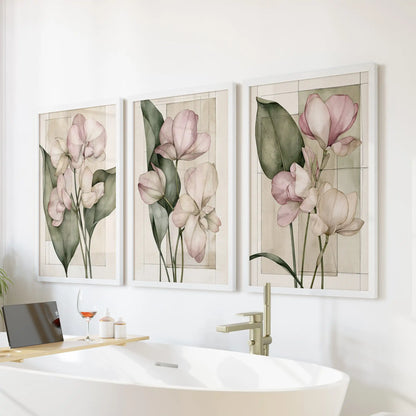 Pale pink flower prints hang in three white frames above a freestanding bathtub.