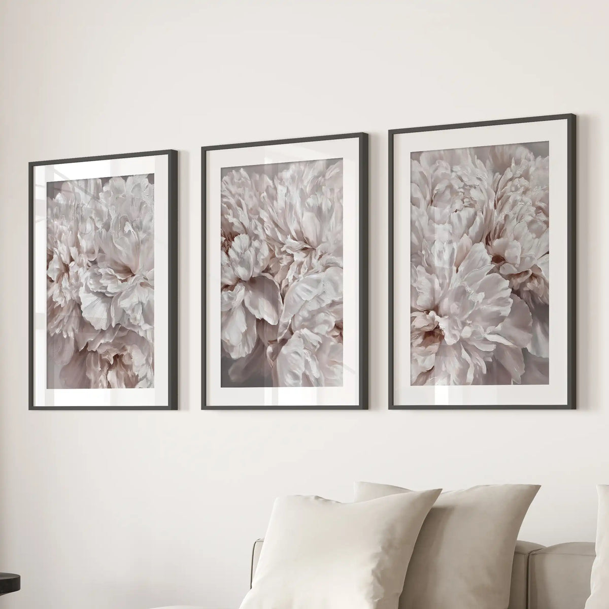 A set of three blush peony close-up prints in black frames with white mats above a sofa.