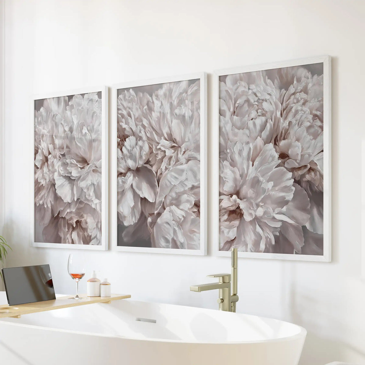Soft pink peony petals and taupe shadows fill three white-framed prints above a freestanding bathtub, with the blooms cropped at the edges.