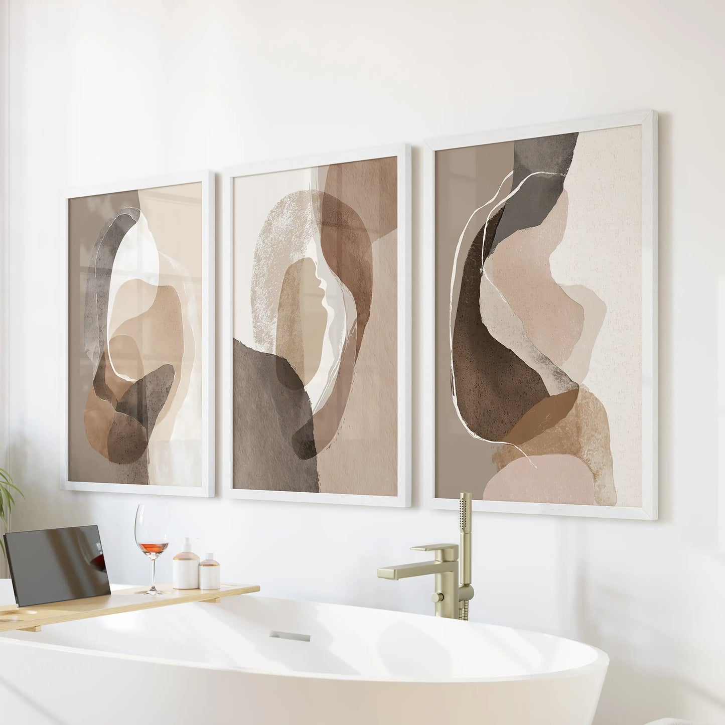 Rustic earthy color blocks trio of wall prints, in crisp white frames, hangs above the tub wall to warm a bathroom with quiet beige and brown hues.