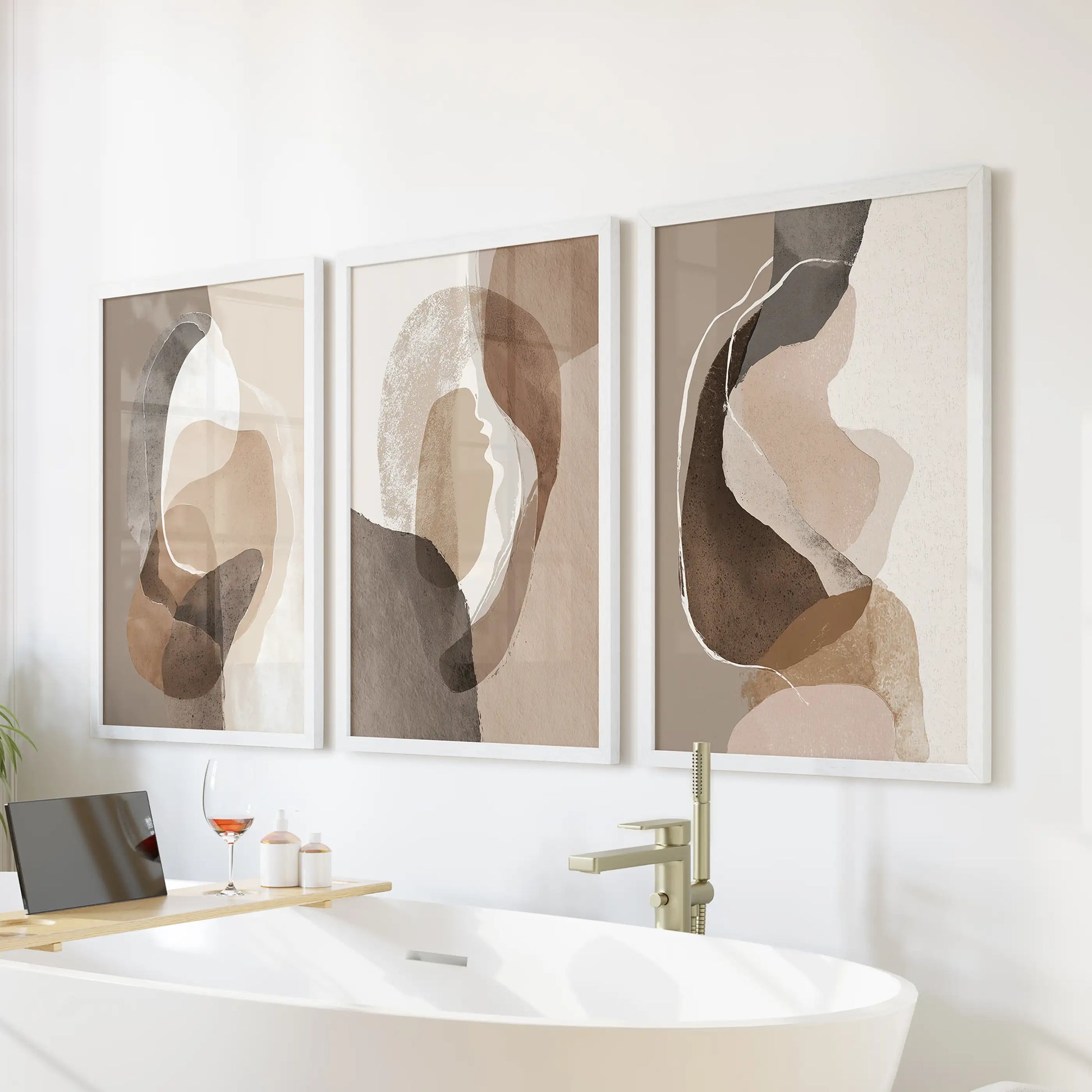 Rustic earthy color blocks trio of wall prints, in crisp white frames, hangs above the tub wall to warm a bathroom with quiet beige and brown hues.
