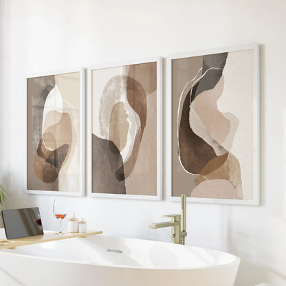Rustic earthy color blocks trio of wall prints, in crisp white frames, hangs above the tub wall to warm a bathroom with quiet beige and brown hues.
