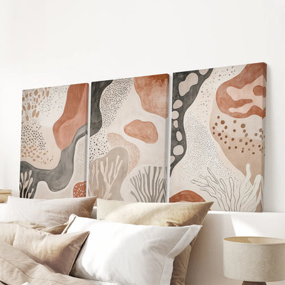 Unframed canvas trio of warm neutral abstracts forms a clean gallery moment above the bedroom headboard.