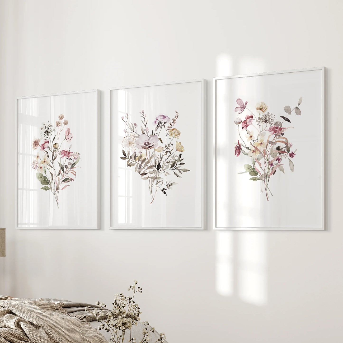 Three white-framed boho botanical prints line the wall beside the bed, softening the bedroom with natural form and texture.