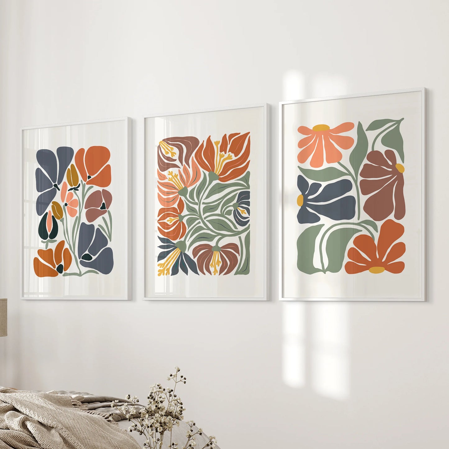 A three-piece set of white-framed terracotta florals infuses the bedroom wall beside the bed with soft boho rhythm and warmth.
