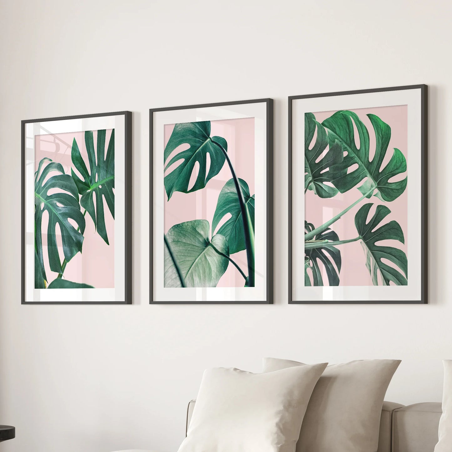 A boho botanical wall trio of monstera prints, matted and black-framed, centers the living-room wall above the sectional in tidy balance.