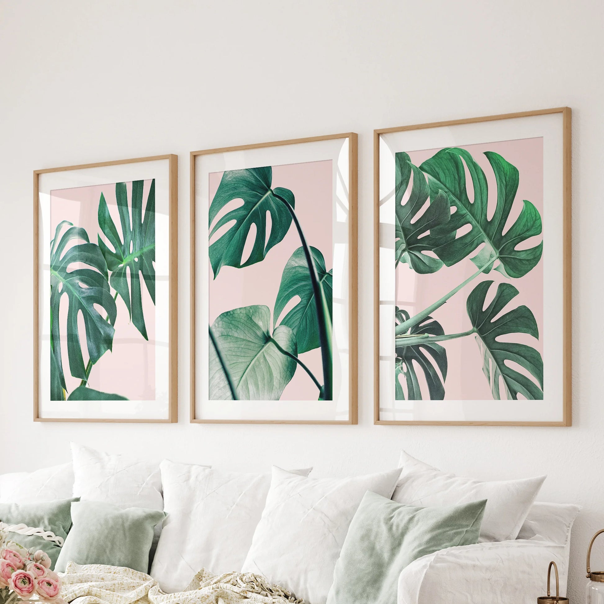 Wood-matted monstera leaf prints in a three-piece set span the living-room wall above the couch, offering crisp boho-tropical style.
