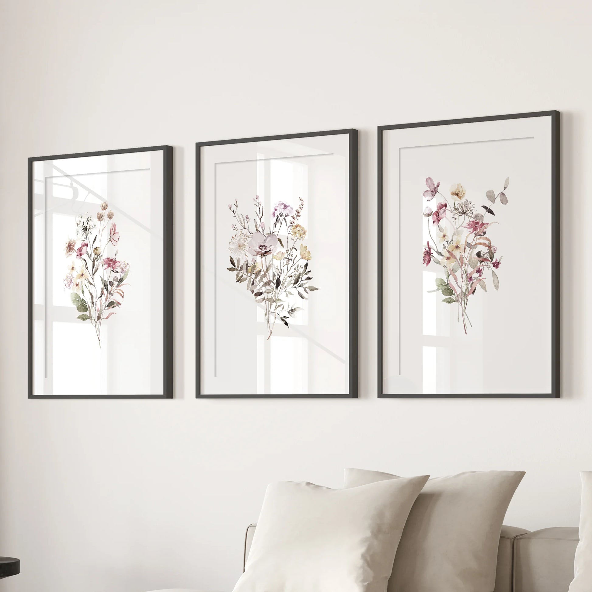 Botanical florals, three wall art prints in black frames with matting, arranged behind the sofa to ground a relaxed living room.