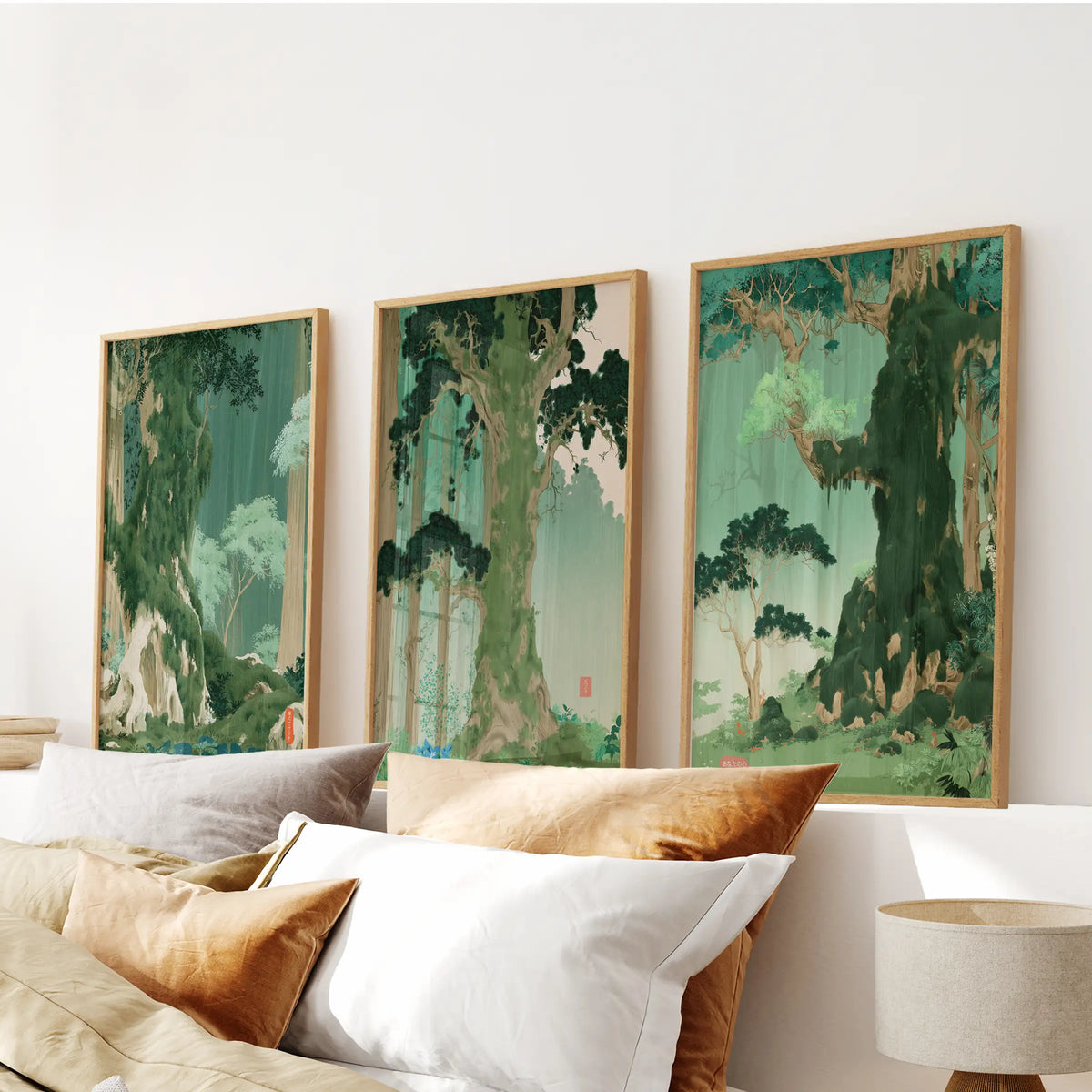 A set of three green botanical scenery art prints in light oak frames hangs above the headboard in a bedroom.