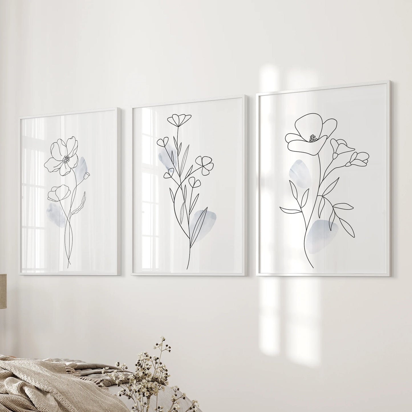Three white-framed botanical line drawings mount beside the bed, giving the bedroom wall a spare, modern softness.