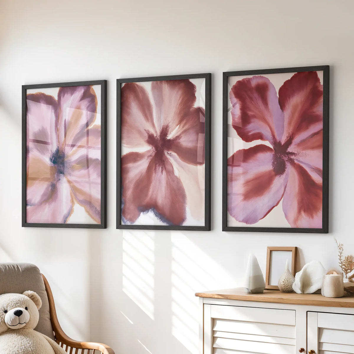 A set of three burgundy and mauve flower prints in black frames above a dresser in a kids' room.