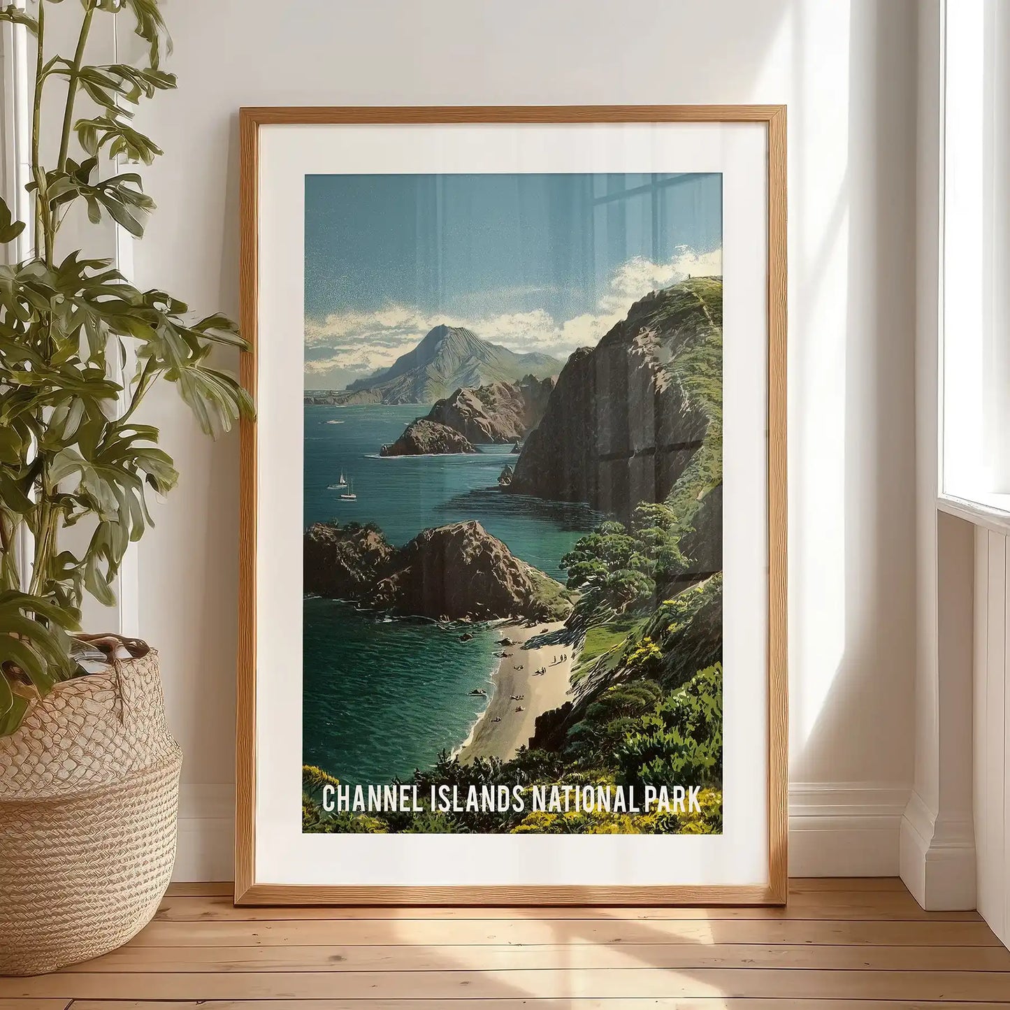 A framed coastal cliffs print with white mat rests on the bedroom floor near the window, the rugged shore and blue water catching daylight.