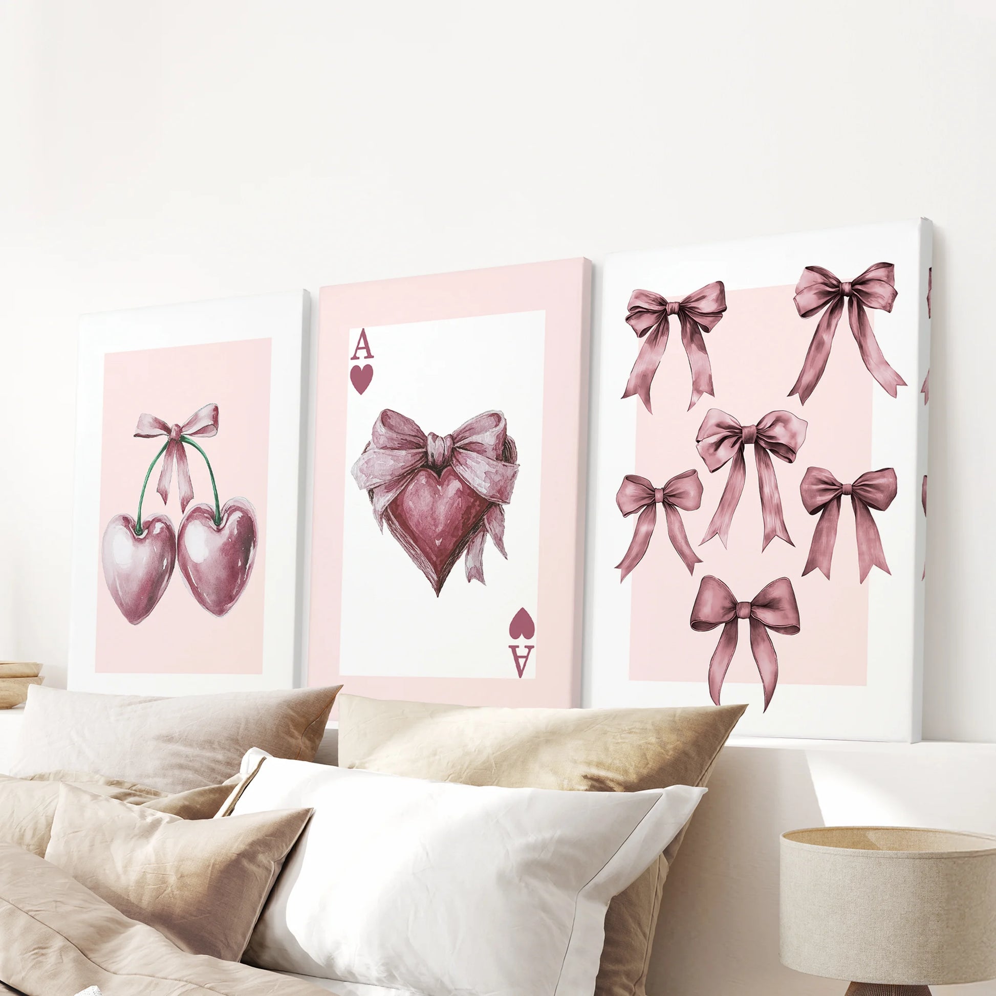 Unframed canvas pieces show the coquette pink icons-ace, bows, and cherries-stacked above the headboard as a lively three-piece wall art display.