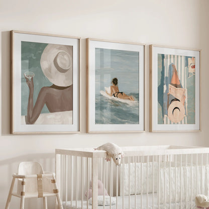 Designer fashion print trio in oak frames with mats, displayed above a bassinet in a nursery.