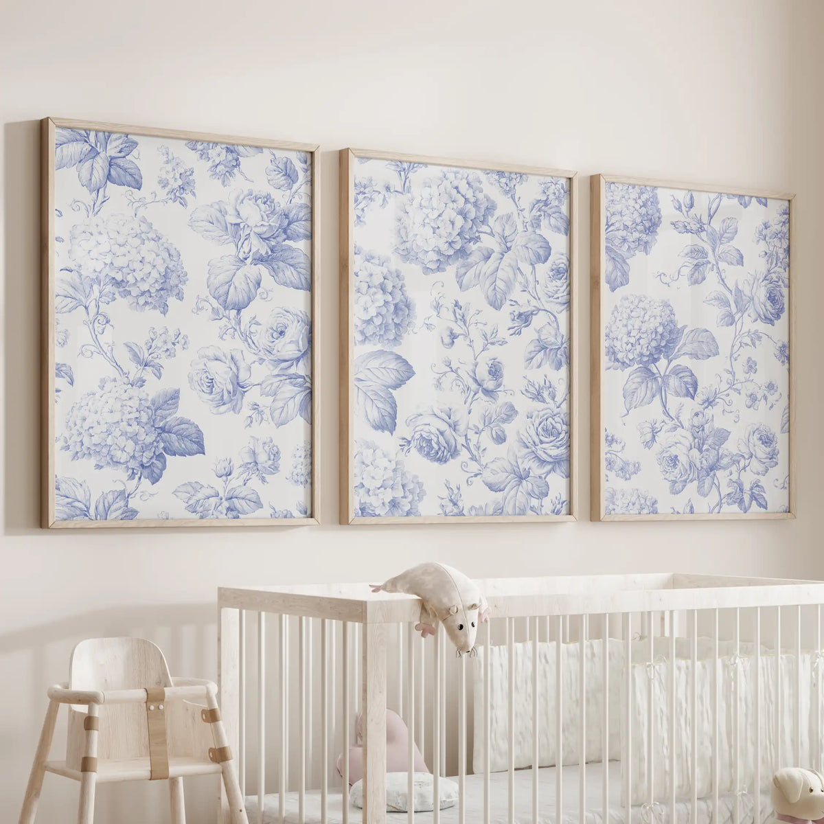 Blue flower patterns fill three oak-framed prints above a nursery crib.