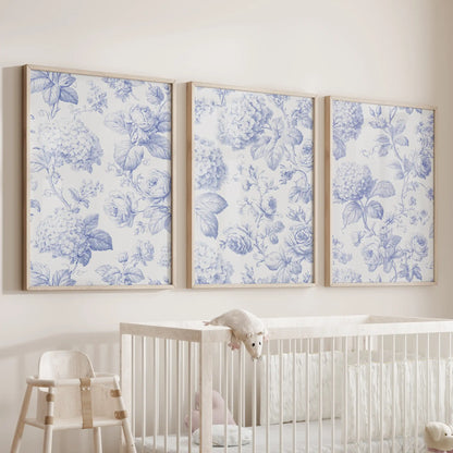 Blue flower patterns fill three oak-framed prints above a nursery crib.