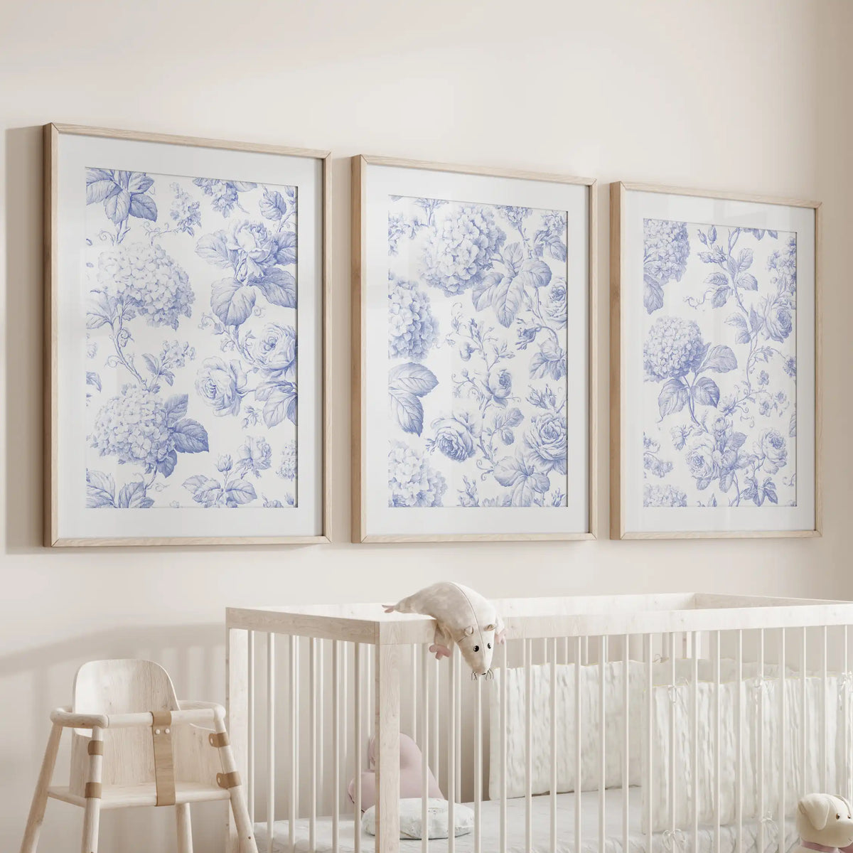 Above a crib hangs a set of three prints showing blue hydrangea clusters and roses on cream backgrounds, framed in oak with white mats.