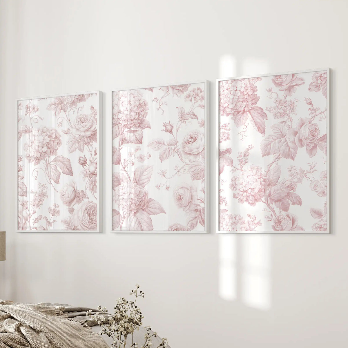 Beside a bed, white frames hold three pink floral pattern prints.