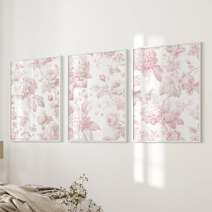 Beside a bed, white frames hold three pink floral pattern prints.