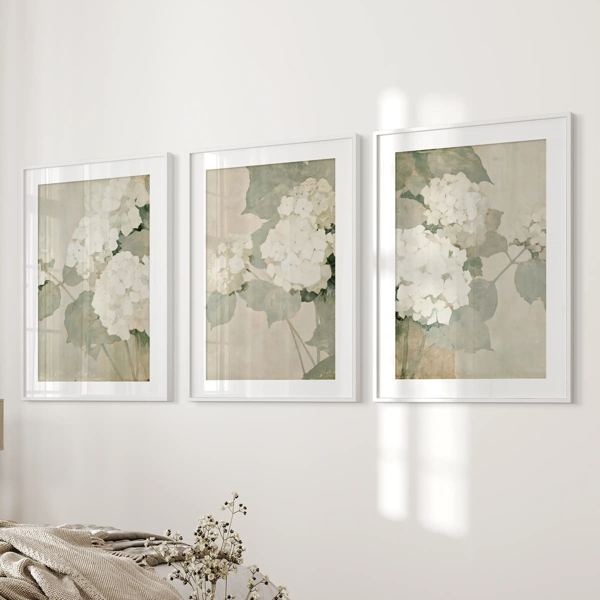 Three-piece wall art set of neutral hydrangea blooms in white matted frames, hanging beside the bed in a bedroom.