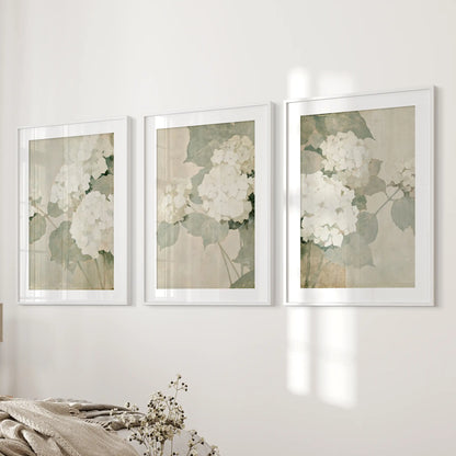 Three-piece wall art set of neutral hydrangea blooms in white matted frames, hanging beside the bed in a bedroom.
