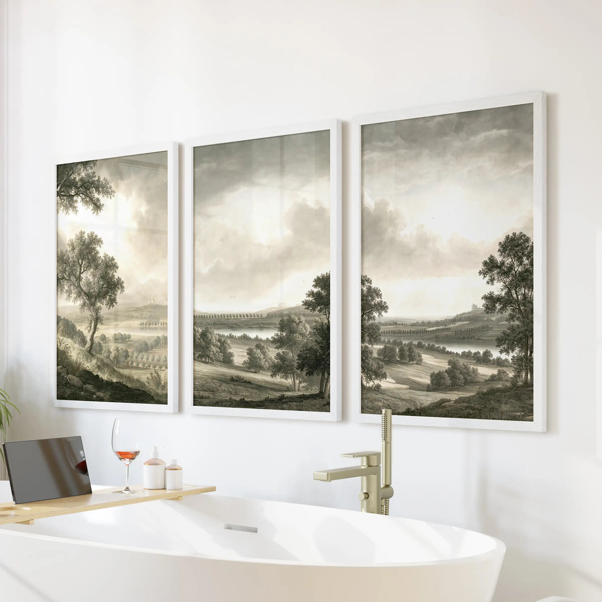 Three-piece trees and fields wall art in white frames, displayed above a freestanding soaking tub in a bathroom.